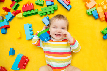 Little baby playing with lots of colorful plastic blocks constructor on a yellow background.