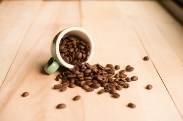 Roasted coffee beans spilled from a cup on a wooden background
