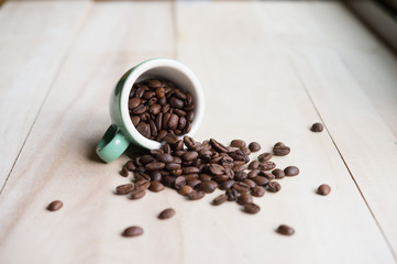 Roasted coffee beans spilled from a cup on a wooden background