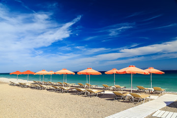 White wooden walkway on beach including umbrellas with deck chairs. Aegean Sea. Greece Rhodes. pebble beach