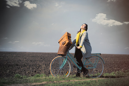 beautiful young woman sitting on the bicycle with suitcase on the wonderful field