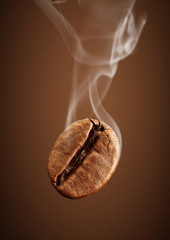 Closeup falling coffee bean with smoke on brown background - obrazy, fototapety, plakaty