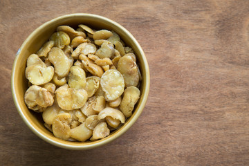 Salted broad beans in bowl on wooden background.