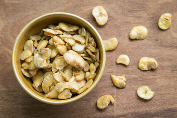 Salted broad beans in bowl on wooden background.