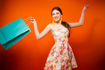 Portrait of young happy smiling woman with shopping bags. Orange background
