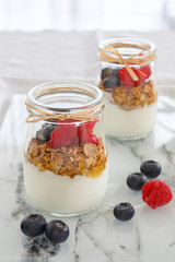 breakfast with yogurt and cereal flakes and raspberries with blueberries. a mixture of yogurt, cereal, berries in a glass jar batch. Rustic food background