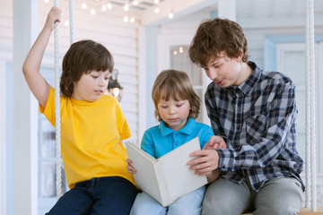 Obraz premium 3 boy read book outdoors on swing