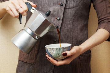 Preparing a cup of strong freshly brewed espresso coffee using a coffee geyser of the beverage pouring into a white cup on a dark shadowy background.