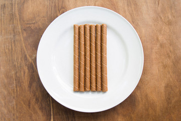 wafer rolls with chocolate in white plate on wooden table.