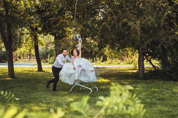 Just married. Bride and groom fooling around riding on the shopping cart