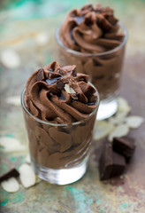 Chocolate mousse with chocolate sauce and chocolate pieces, almond slices in a glasses on a vintage background.