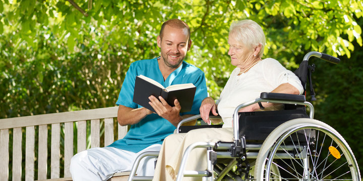 Carer reads a book to the elderly persons