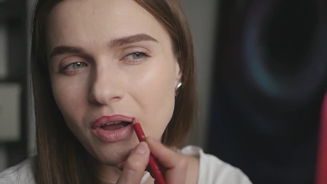 attractive young girl sitting in front of a mirror paints lips with a red pencil line, slow motion