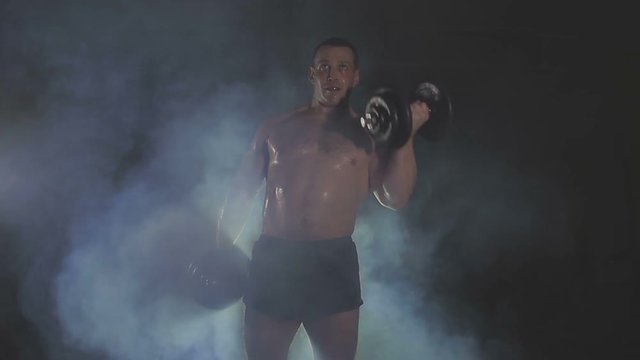 Strong sportsman lifting heavy dumbbells in smoke