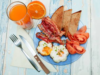 Fried eggs with toast, bacon and tomato on a plate