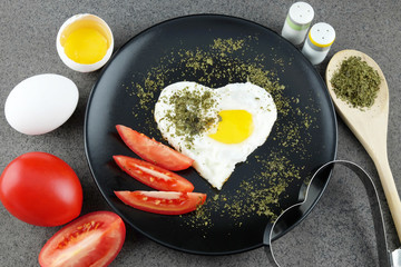 Fried egg in shape of heart on black plate.