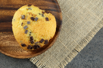 Muffin with chocolate chips on wooden plate.