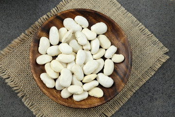 Dried white beans on wooden plate on sachckolth.