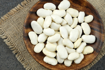 Dried white beans on wooden plate on sachckolth.