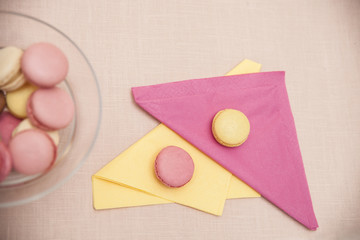 Yellow and pink macaroons french sweets on yellow and pink napkins with colorful macarons (macaroons) in a glass bowl in the background from above.