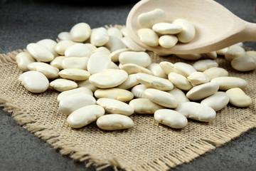 White dried beans and a wooden spoon on burlap.
