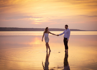 Fototapeta premium Happy loving couple in white dresses walking in water