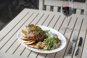 Leg of lamb baked with sauce in the white plate closeup with a side dish of rice. Rustic wooden table and a glass of red wine.