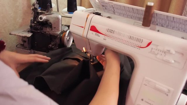 Seamstress work on the sewing machine. Girl sits at the table and scribbling on the sewing machine.