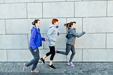 Three attractive sportswomen running against a concrete wall
