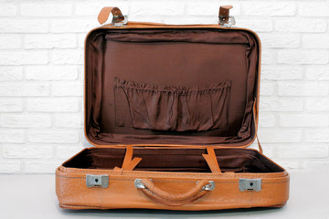 Old open suitcase against a white brick wall