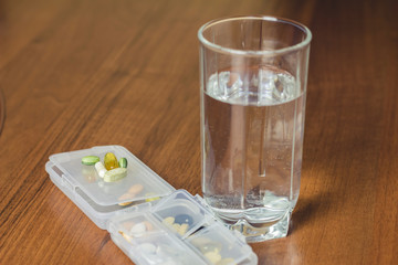 Mixed natural food supplement and vitamin pills, glass of water on wooden table.