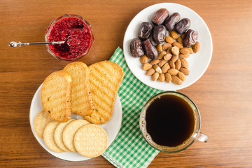Breakfast time, cup of coffee with toasts, raspberry jam, dates, almonds on wooden table, top view.