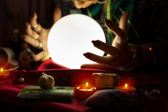 Illuminated crystal ball and hands of fortune teller woman