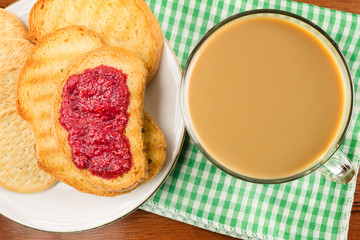 Breakfast time, cup of coffee with milk and toasts with raspberry jam on napkin, top view.