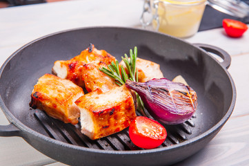 Close up bbq chicken breast with vegetables in a frying pan on the white wooden background with details. Selective focus