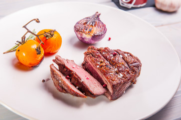 Close up Grilled beef tenderloin steak with grilled onion and cherry tomatoes on the white plate on the wooden background with details. Selective focus