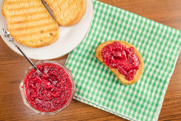 Breakfast time, toasts with raspberry jam on napkin, at wooden table, top view.