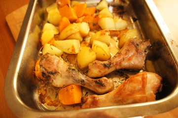 Roasted chicken legs on metal plate with potatoes and pumpkin 