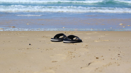Black slippers on the sand beach with relaxing waves