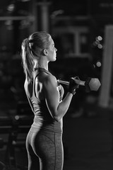Beautiful sporty woman doing power fitness exercise at sport gym. Girl with dumbbell. Black and white.