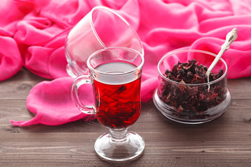 Transparent cup of Hibiscus tea on a background of dry tea