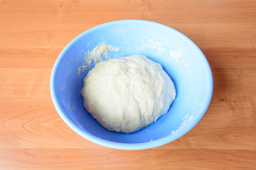 Yeast dough ready to bake. Raw materials for baking. Bowl with dough on the wooden table.
