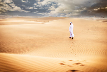 Arabic man with traditional emirates clothes walking in the desert