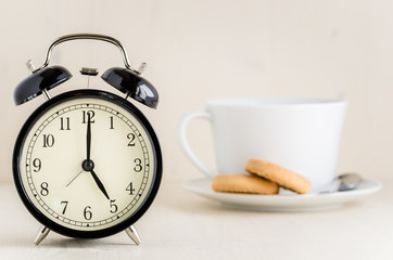 Vintage Black Alarm Clock with a White Tea Cup with Biscuits in Background