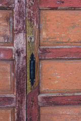 Old painted wooden door in warm colors with iron handle.