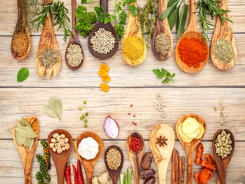Various of spices and herbs in wooden spoons. Flat lay of spices ingredients chilli ,pepper corn, garlic, thyme, oregano, cinnamon, star anise, nutmeg, mace, sage and parsley on the wooden background.