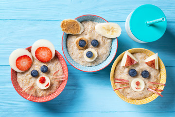 Funny bowls with oat porridge with cat, dog and mouse faces made of fruits and berries, food for...