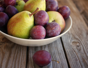 Ripe fresh pears and plums in a bowl on a wooden background close up. Autumn harvest of fruit.
