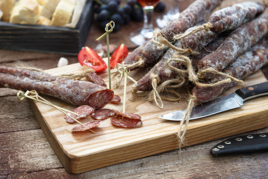 Bread, sausage, red wine, glass, cutting board and knife arranged on a wooden table for a snack in the countryside.