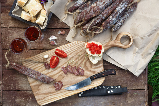 Bread, sausage, red wine, glass, cutting board and knife arranged on a wooden table for a snack in the countryside.